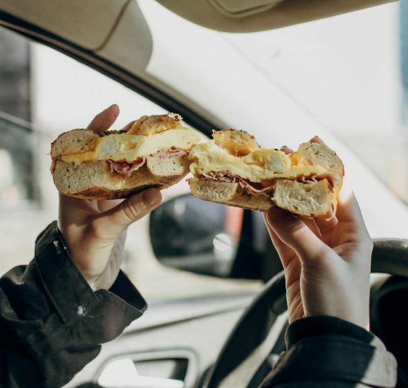 Driver holding up Bagel Breakfast Sandwich in car. 