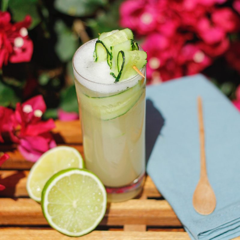 cucumber cocktail sitting next to lime and spoon.