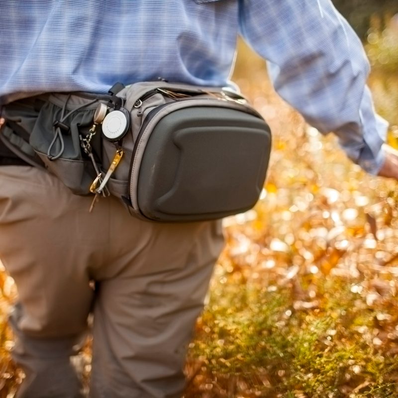 A rear view of a man with a waist pack walking in a field.