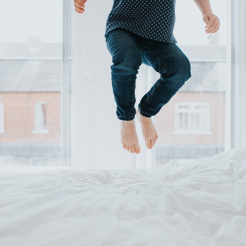 Someone bouncing on a white bed in a bright room.