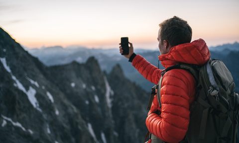 A hiker in puffer jacket taking a picture of the mountain view.