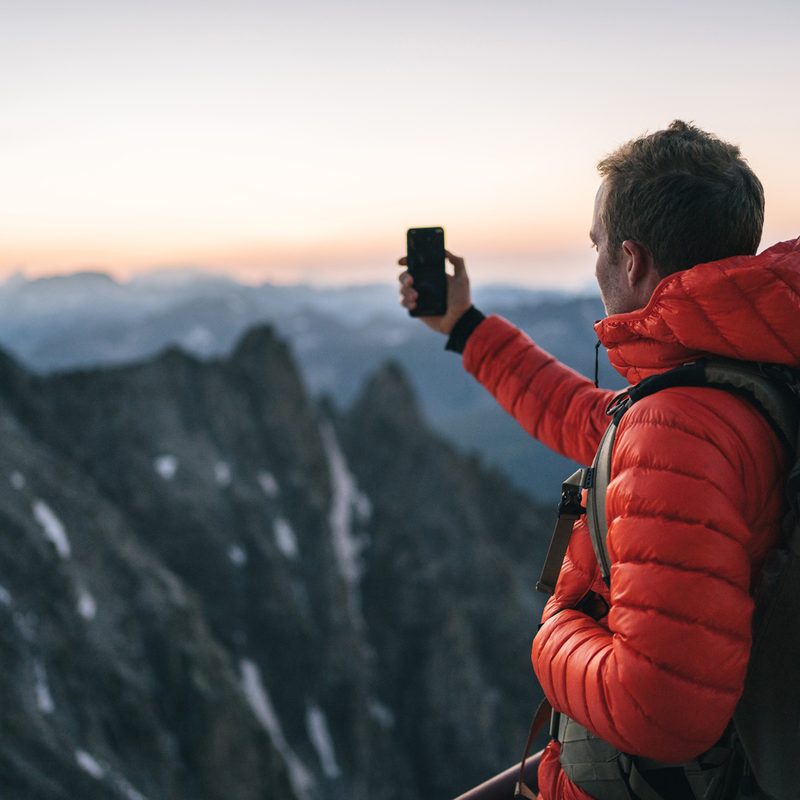 A hiker in puffer jacket taking a picture of the mountain view.