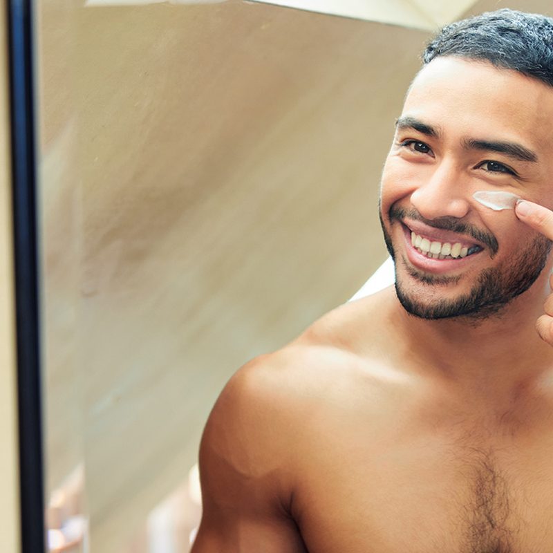 Shot of a young man looking in the mirror while applying moisturizer to his face.