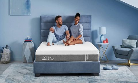 A man and a woman on a Tempur-Cloud mattress in a blue bedroom.
