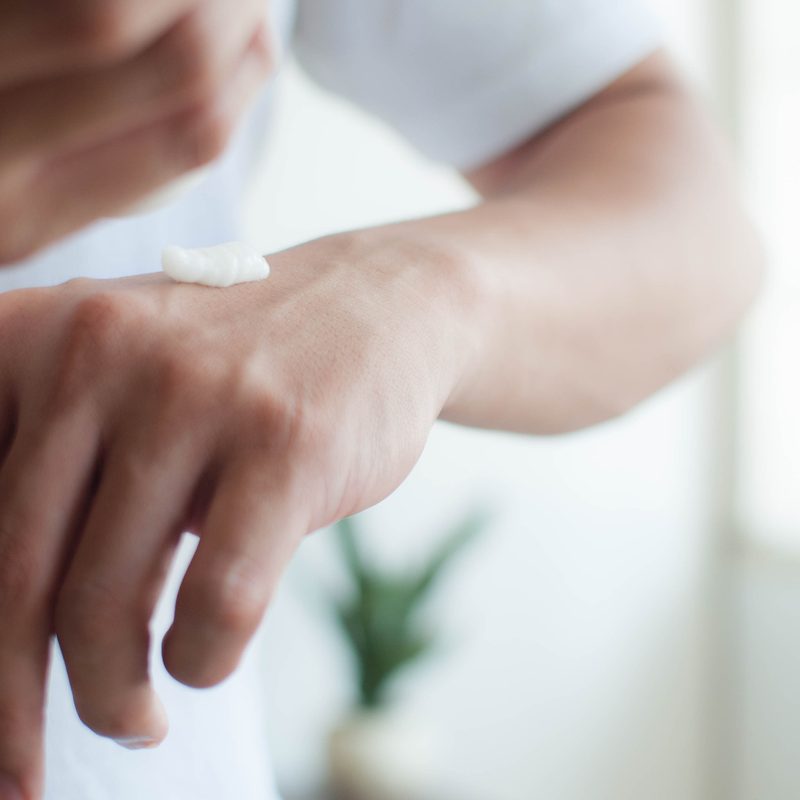 A close-up view of a young man applying lotion to his hands.
