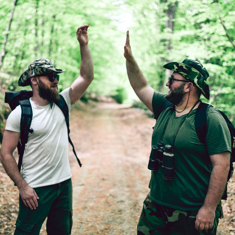Two male hikers making a high five in a forest.