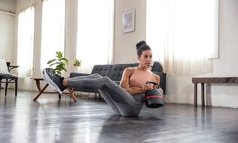 Woman using the Bowflex SelectTech Kettlebell in a twist weight pilated exercise while seated on the floor of her living room.