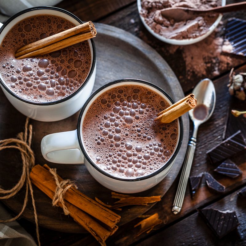 Two homemade hot chocolate mugs on rustic wooden table.