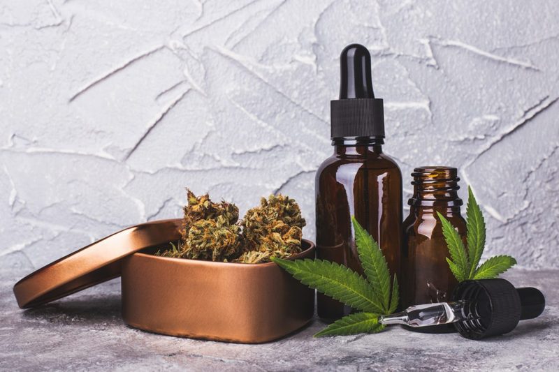 Cannabis oil extracts in droppers beside marijuana leaves and a marijuana cones in a metal container