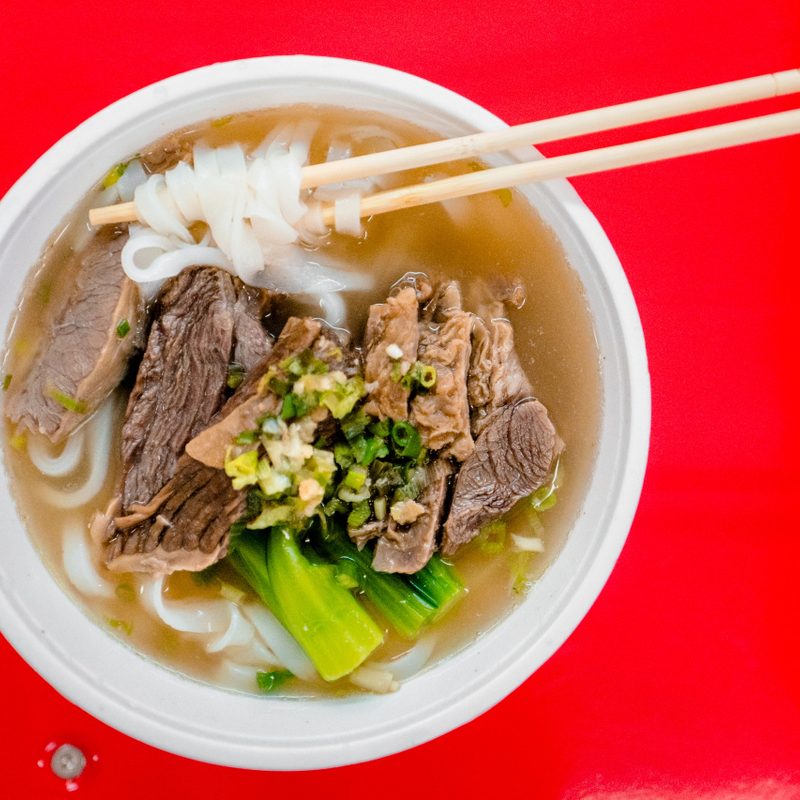Bowl of Chinese brisket noodles with a red background.