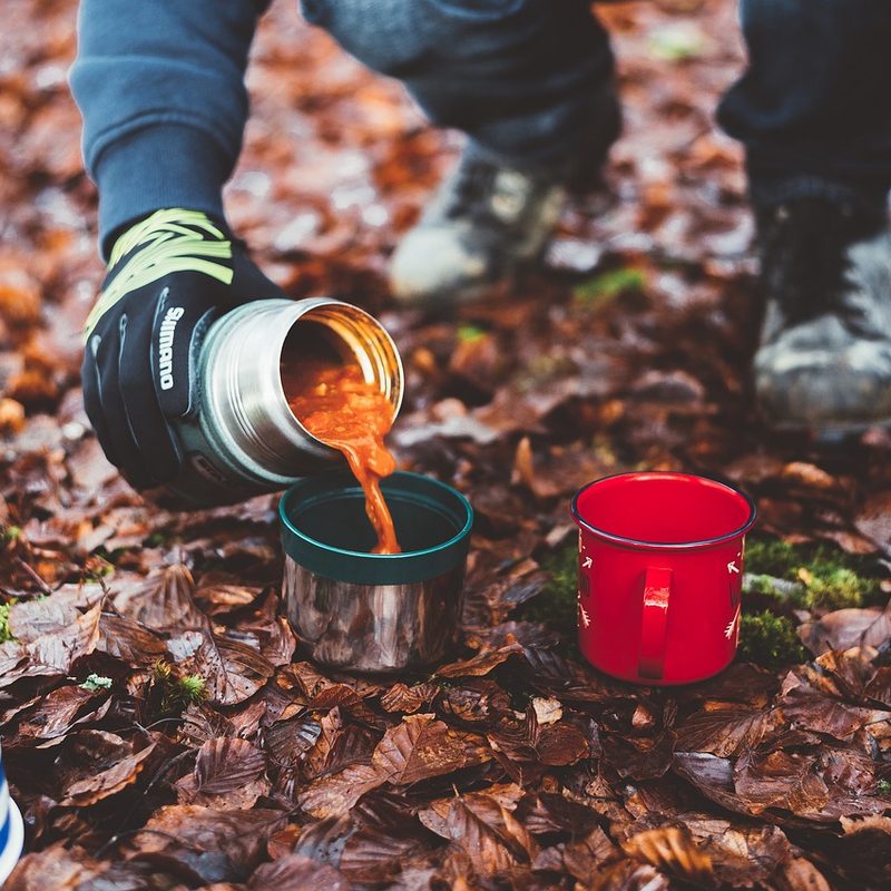 Person pouring coffee from a thermos on a hiking trail.