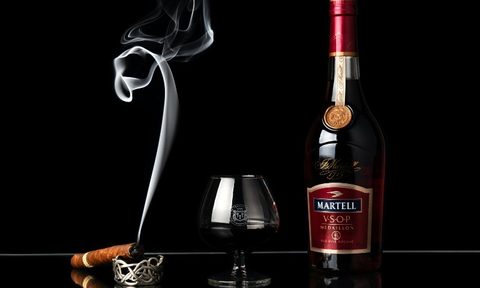 A cognac glass and bottle with a lit cigar.