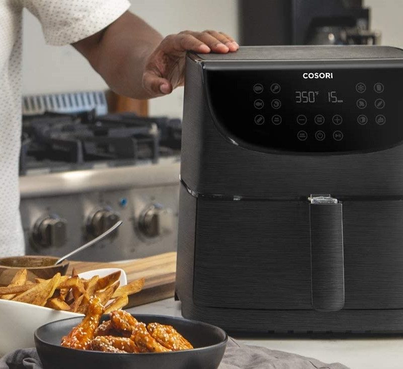 COSORI Air Fryer Max XL on counter with chef cooking.