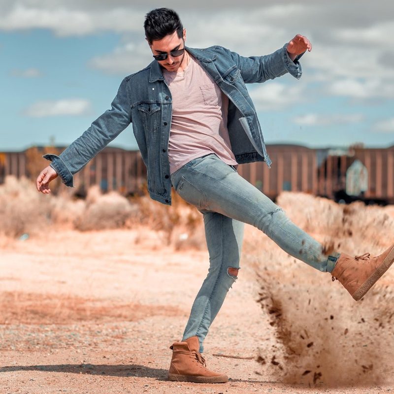 Man in denim and desert boots kicking up sand.