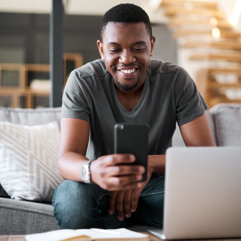 A man on a sofa using his phone and laptop.
