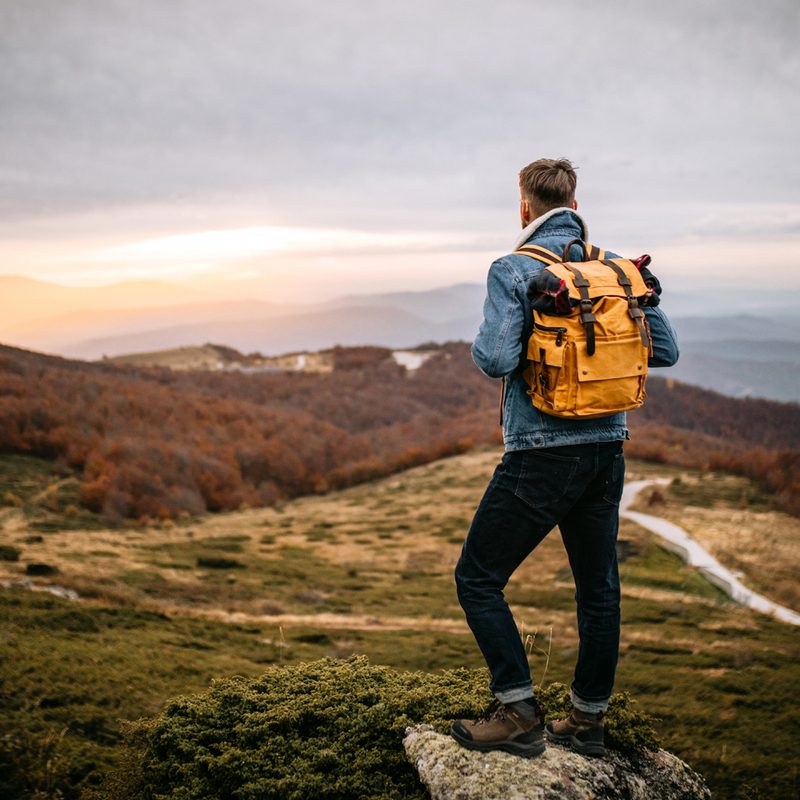 A man carrying an orange backpack enjoying the view from a mountain top.