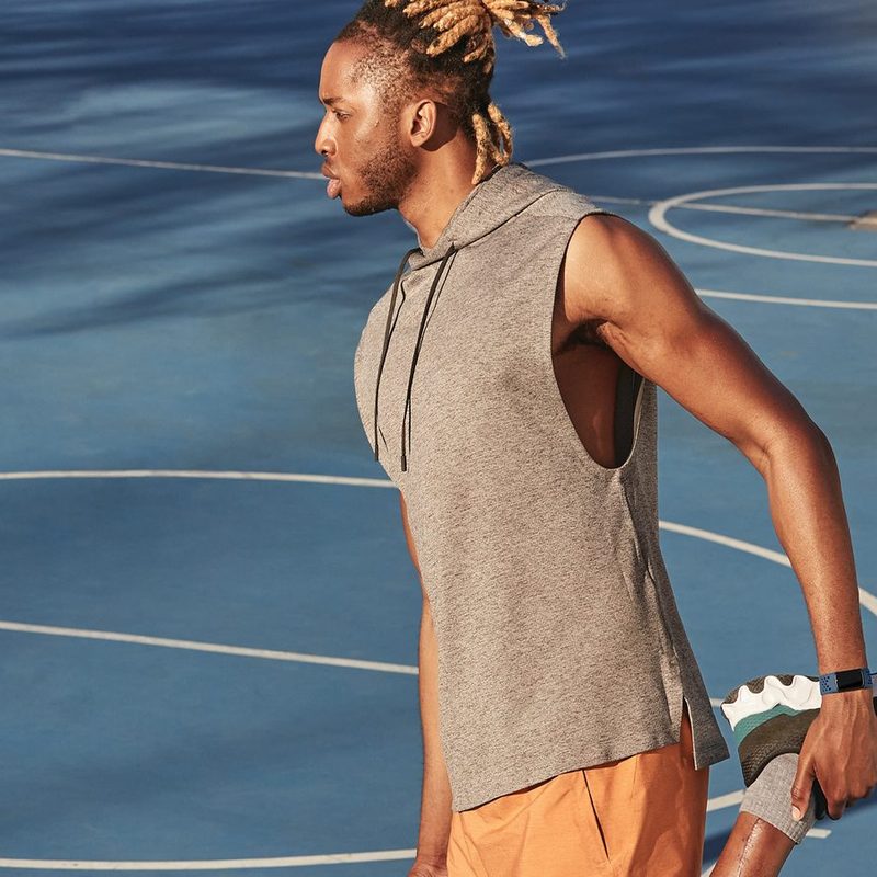 A male athlete with Fitbit tracker stretching at a basketball court.