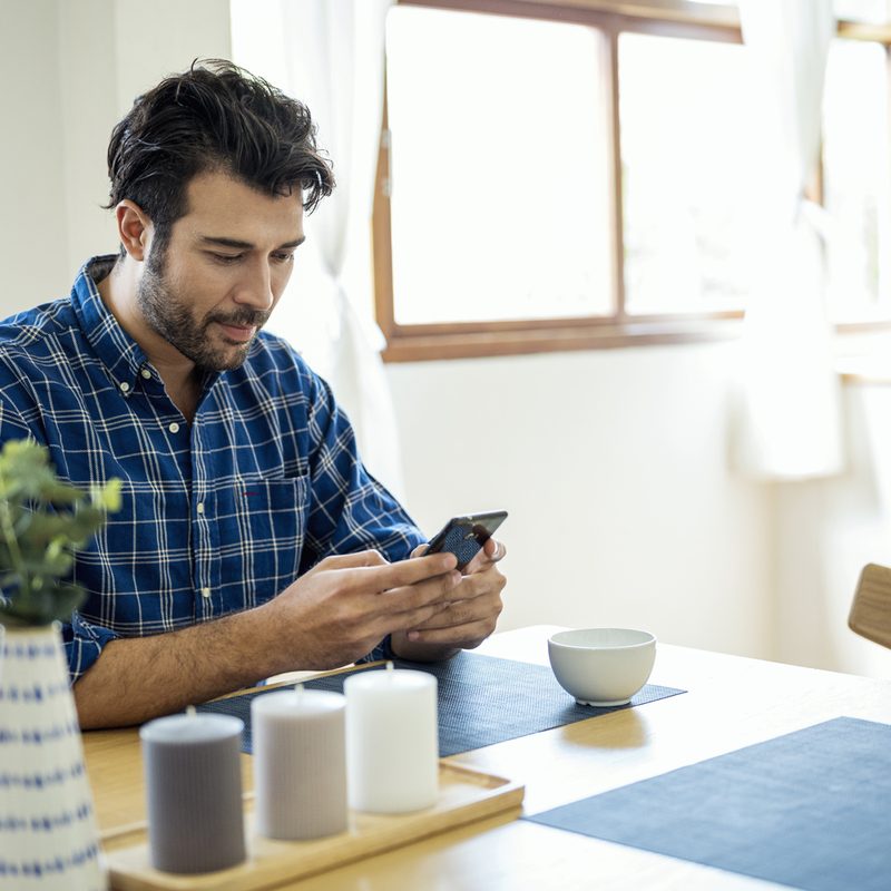 A man using his phone at dining table.