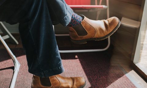 Male wearing Brown Leather Chelsea Boots, legs crossed at the knee, sitting in a sun room