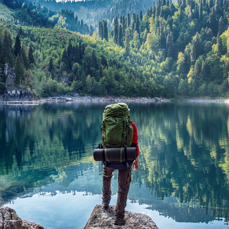 Hiker with a backpack in front of a mountain lake background.