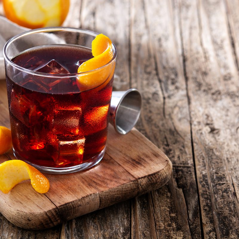 A Boulevardier cocktail with orange skin on a wooden table.