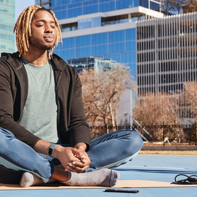 A man with Fitbit tracker meditating in the city.