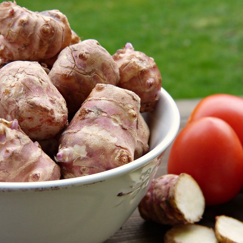 Jerusalem artichokes in a bowl sitting next tomatoes.