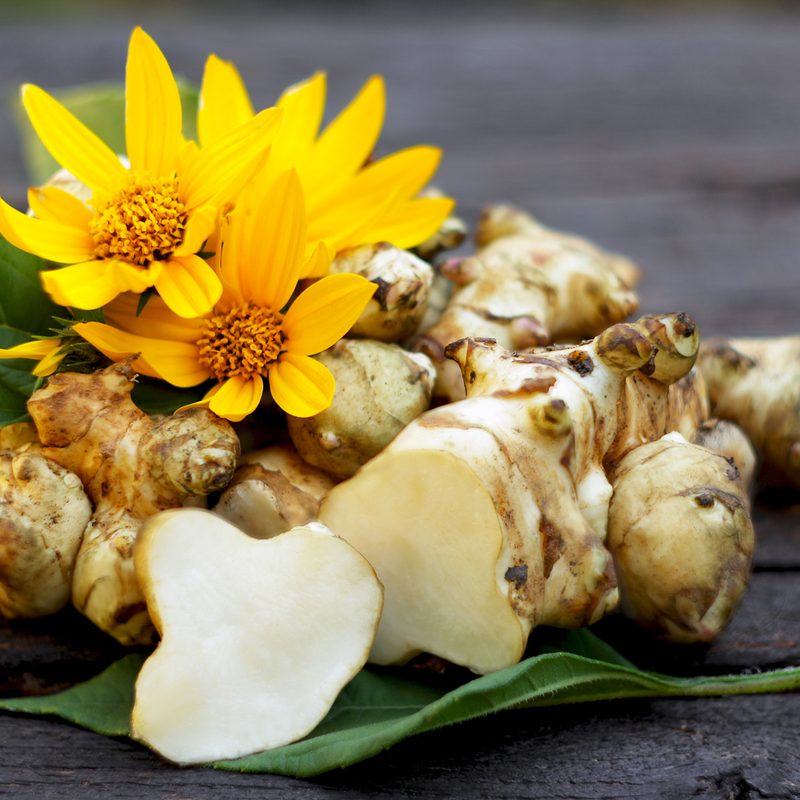 Jerusalem artickoke, flowers, and leaves on a wooden table.