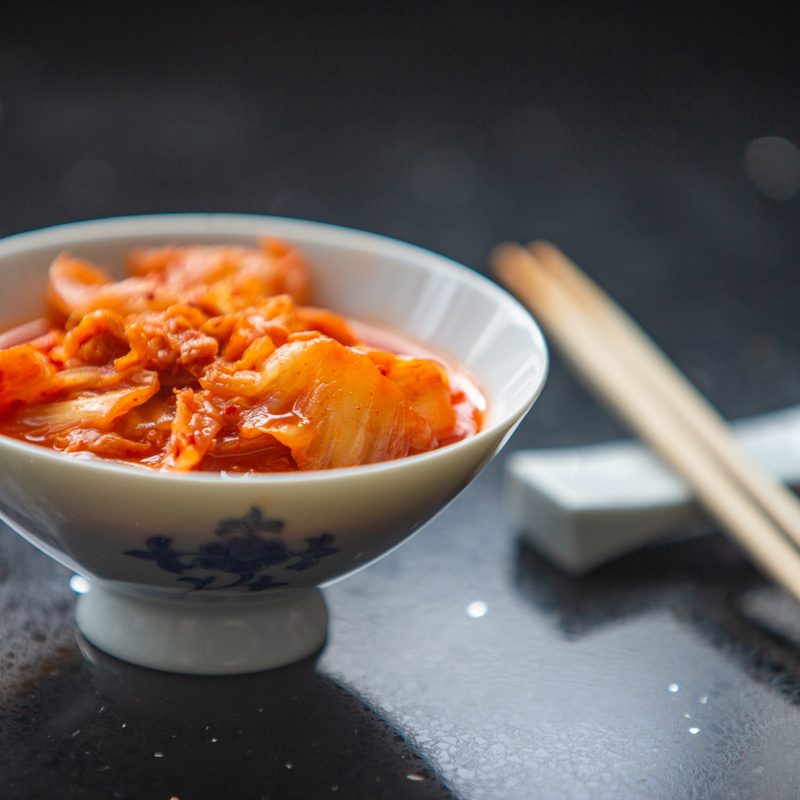 Kimchi served in a porcelain bowl beside a pair of chopsticks.