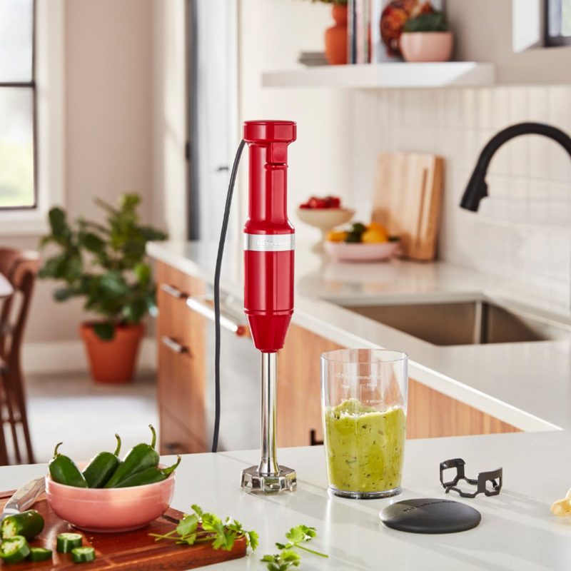 KitchenAid corded hand blender on a kitchen counter next to smoothie and ingredients used to make it.