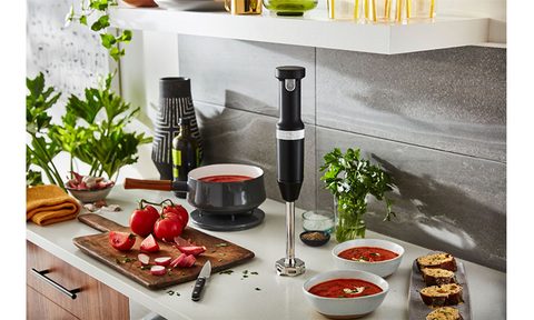 KitchenAid Cordless Variable Speed Hand Blender placed on a kitchen countertop surrounded by food.