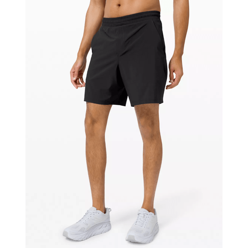A midsection of a man wearing a black Lululemon Pacebreaker Short and white shoes. 