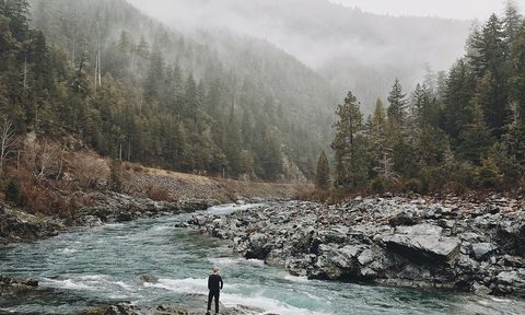 man standing beside rocky river