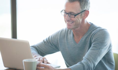 Man wearing a v-neck sweater while using a laptop and having a cup of coffee.