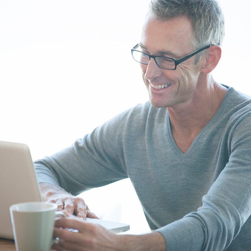 Man wearing a v-neck sweater while using a laptop and having a cup of coffee.