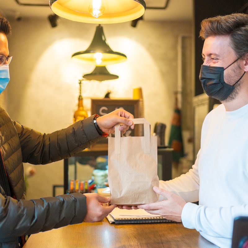 A male barista handing out a paper bag to a customer.