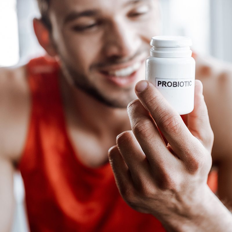 A smiling male athlete looking at a probiotic supplement.