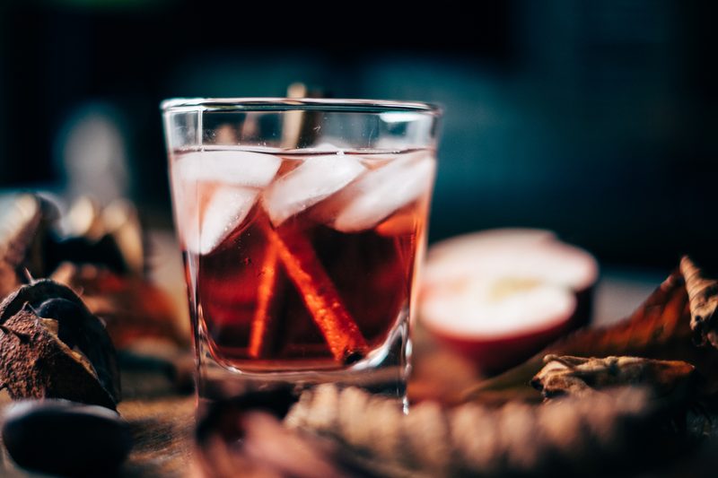 An apple cider cocktail with ice and cinnamon sticks.