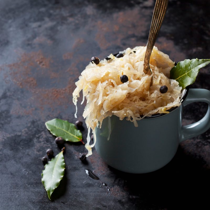 A spoon in a cup of sauerkraut with berries and bay leaves.