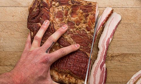 Schaller Weber bacon being sliced on wooden table.