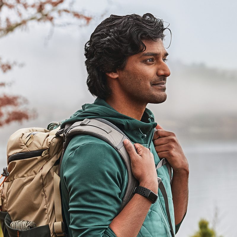 A man with backpack wearing a Fitbit tracker in the outdoors.