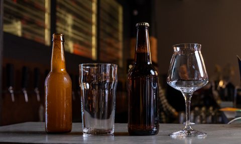 two bottles of beer and two stout glasses on a bar.