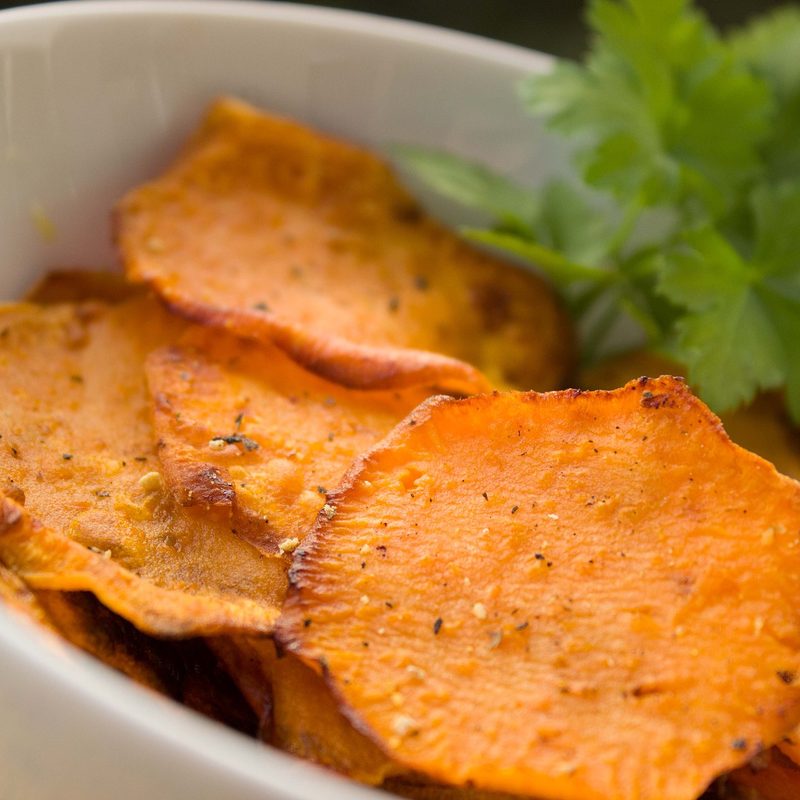 Cooked sliced sweet potatoes in a white bowl bowl with parsley garnish.