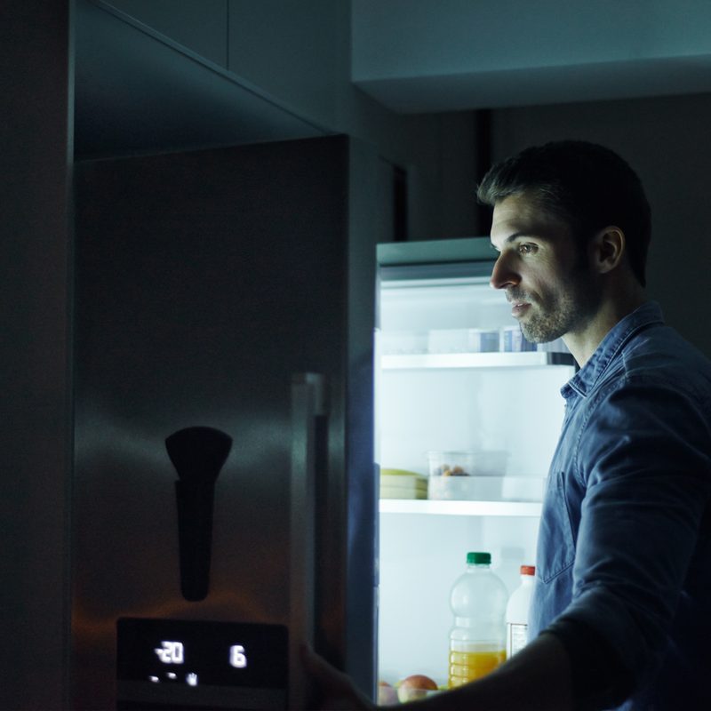 A man looking for something to eat in his fridge at midnight.