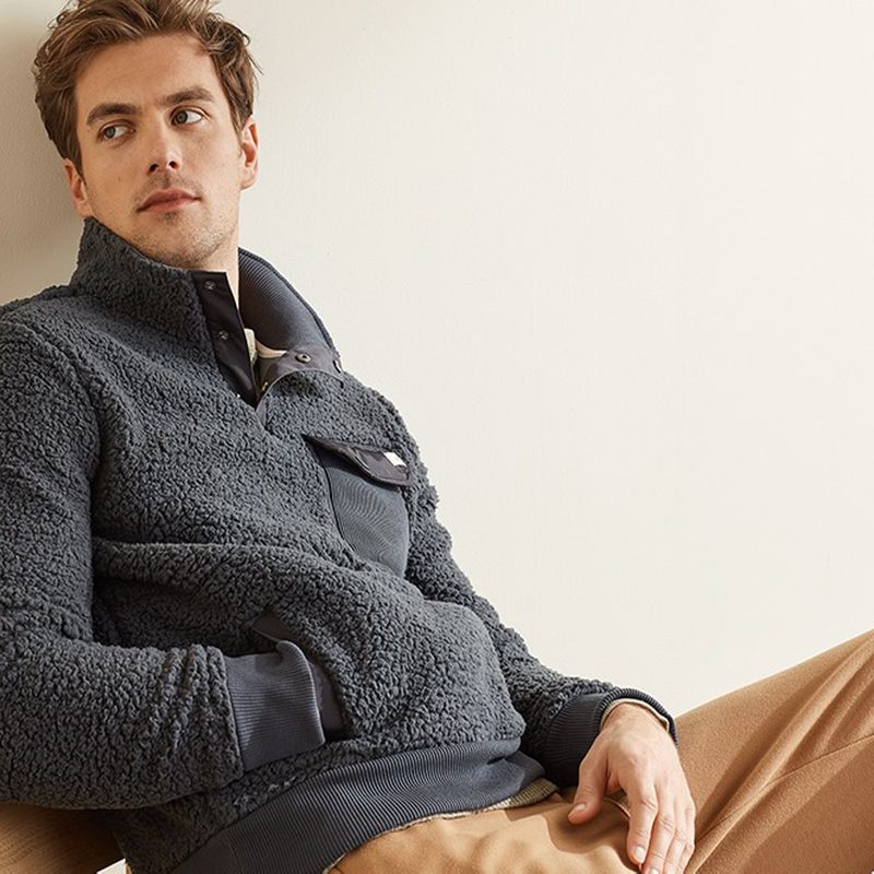 A male model in sweatshirt and pants sitting on a chair.