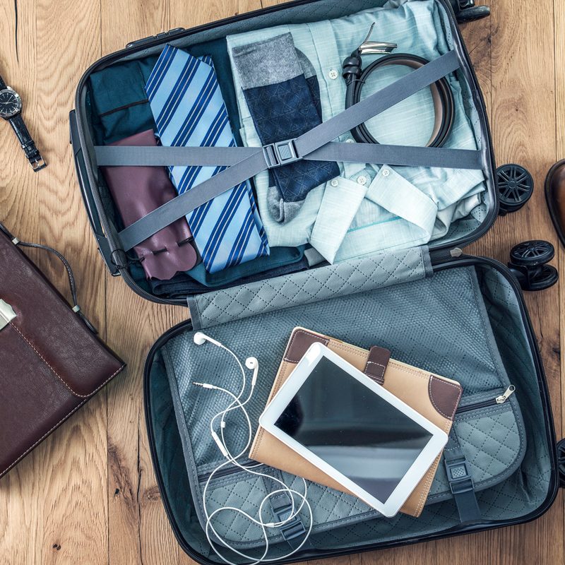 A luggage with iPad and clothes in between a briefcase and a pair of shoes.