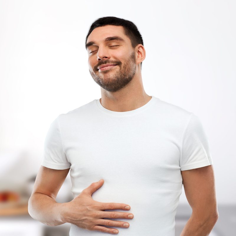 A man in white t-shirt happily touching his stomach.