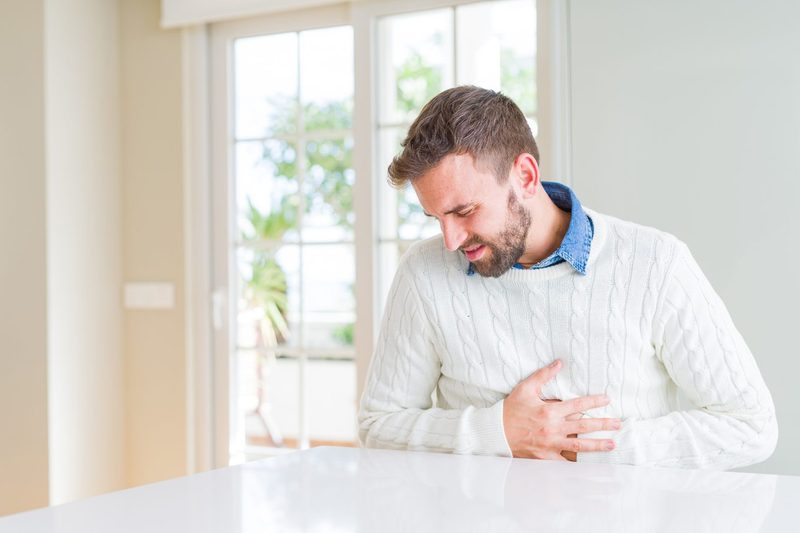 A man in white sweater touching his aching stomach.
