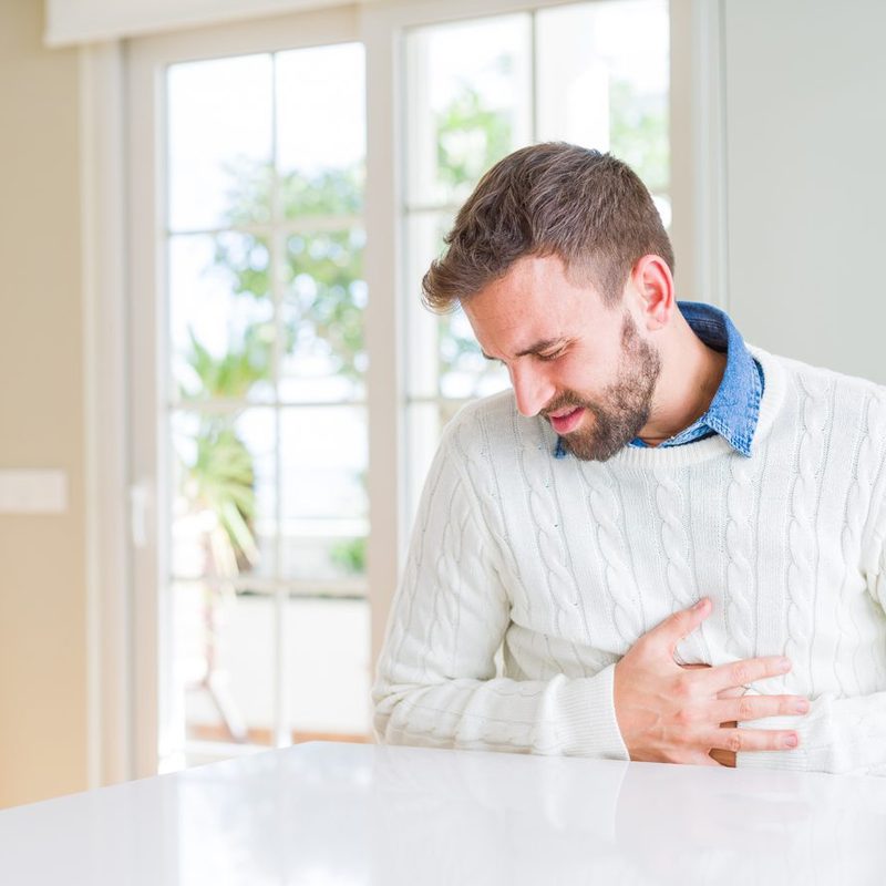 A man in white sweater touching his aching stomach.