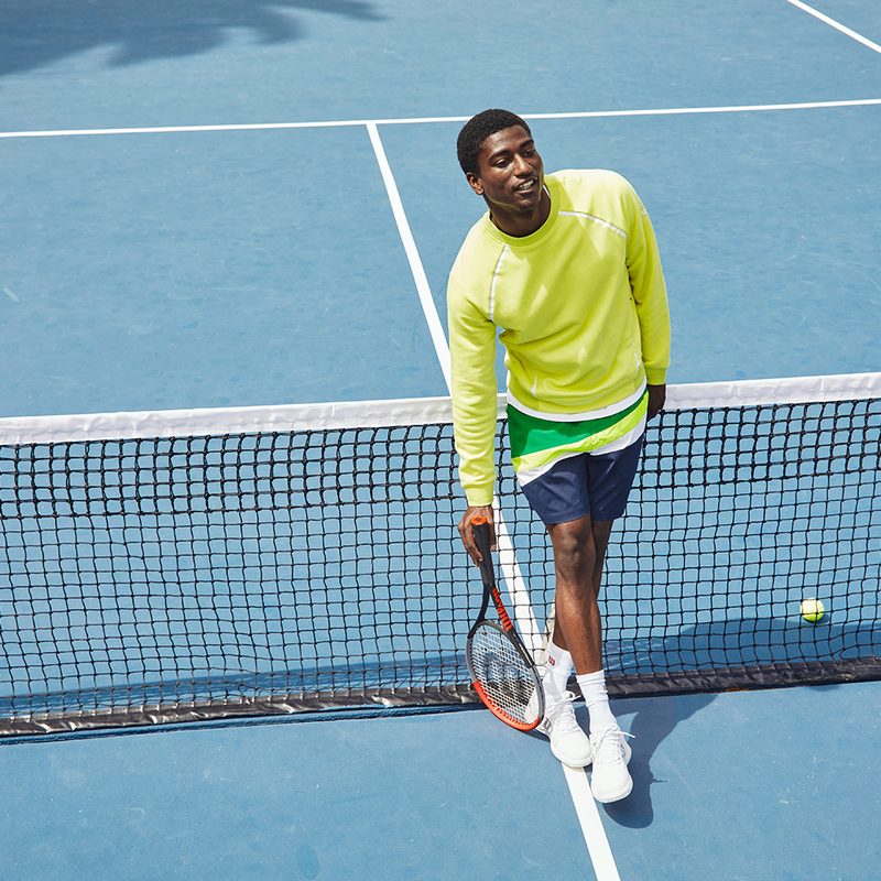 Lifestyle image of man standing on tennis court wearing Wilson sportswear.